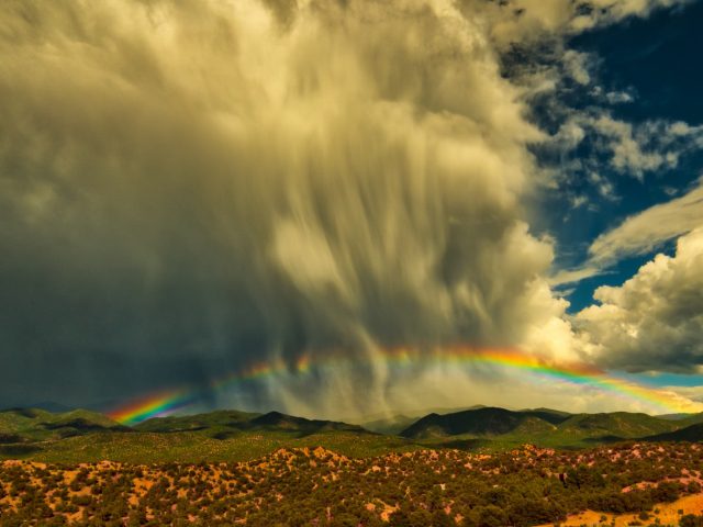 A low rainbow over Tesuque, New Mexico with curtains of falling rain.